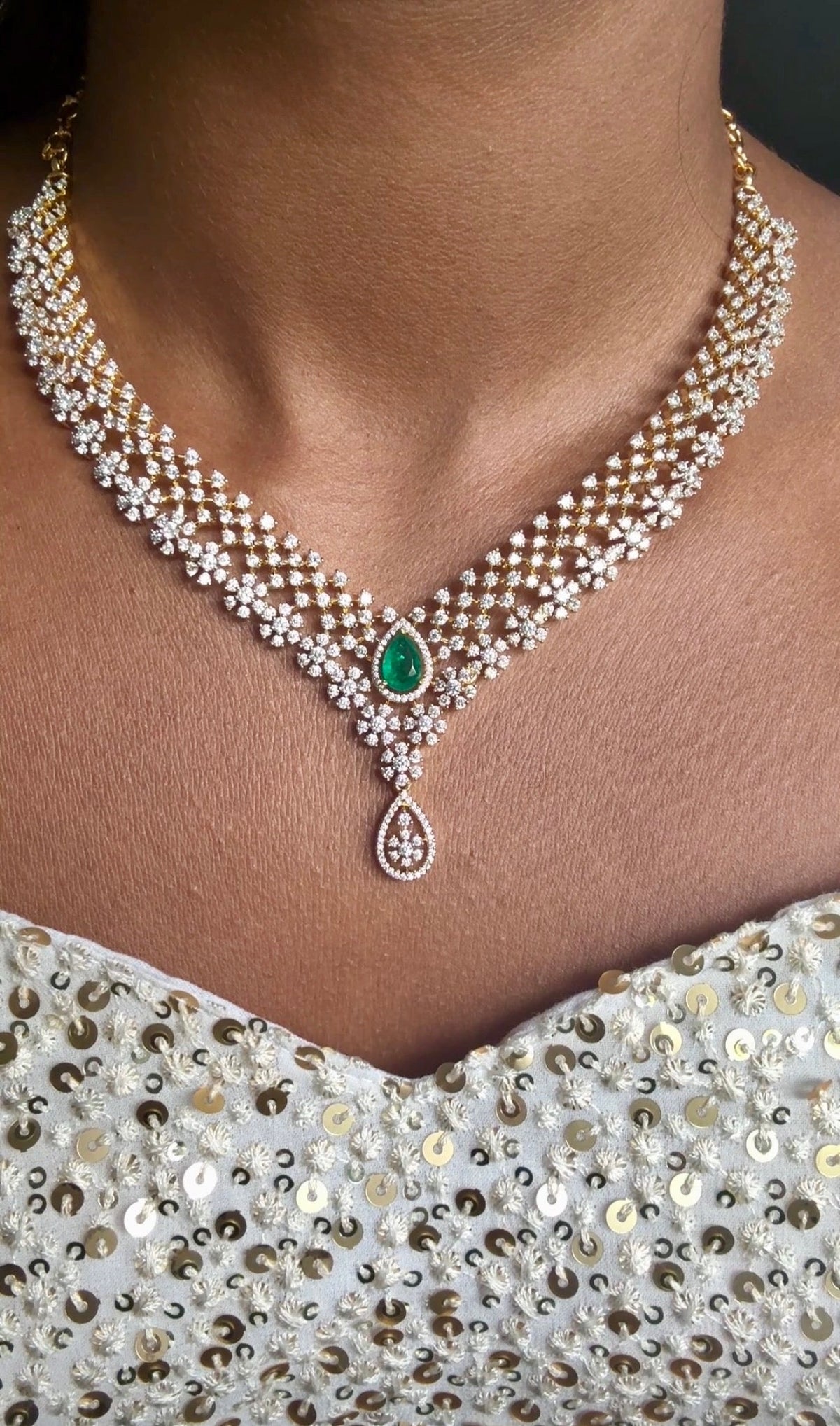 Layered gold-plated cubic zirconia necklace and earring set in emerald green, worn with an embellished outfit